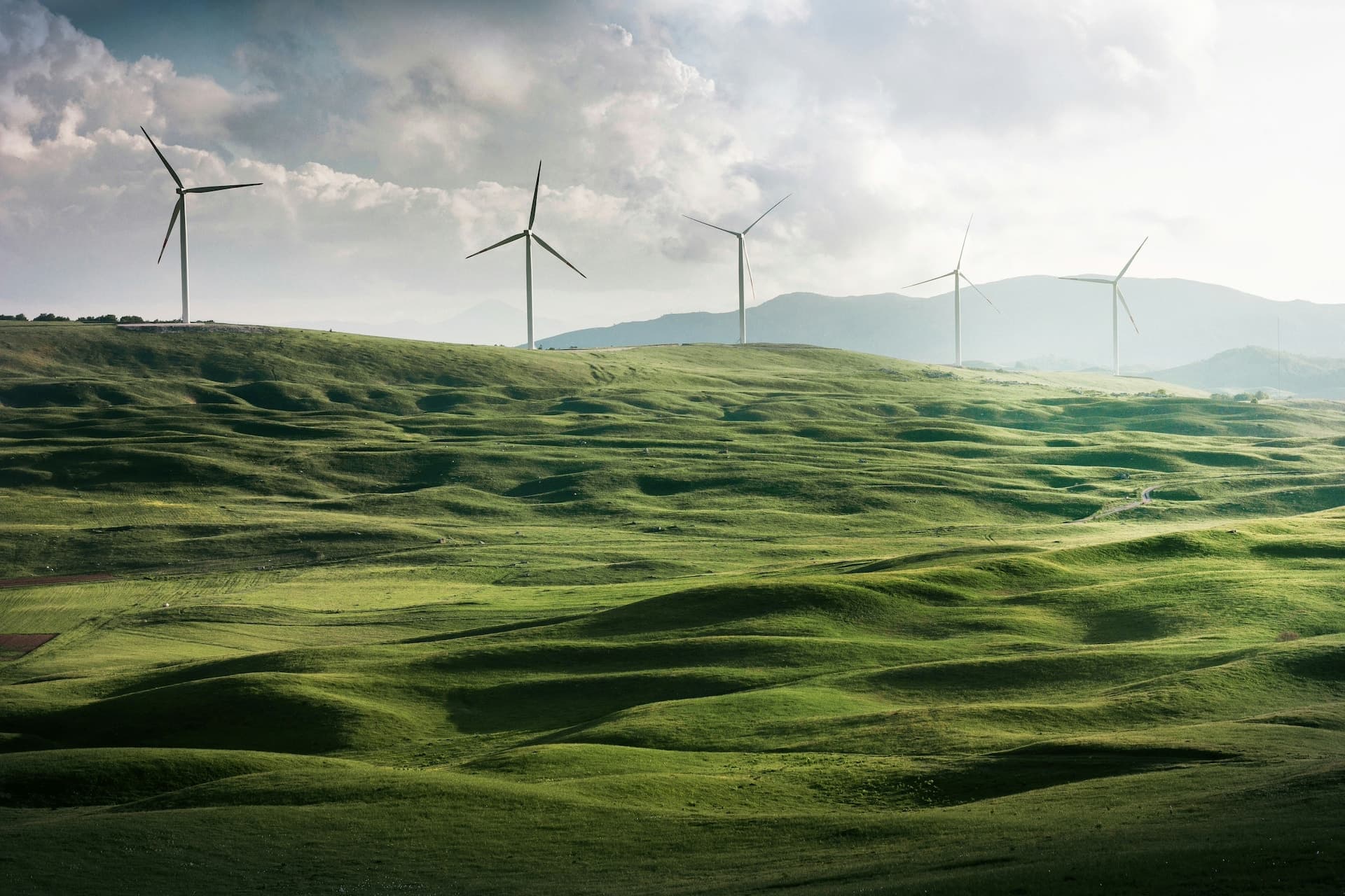 Wind turbines on rolling green hills under a clouded sky